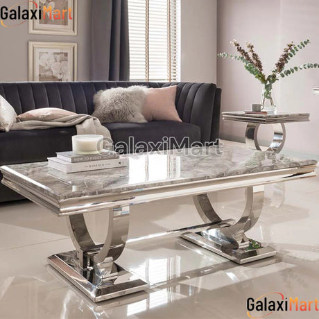 A sophisticated Arianna coffee table with a stainless steel base and a marble top, placed in a living room setting with a couch and decorative items.